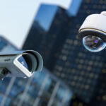 two cctv security camera in a city with blurry business building on background